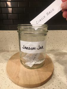 Image of hand depositing a piece of paper that reads circle back into the Jargon Jar